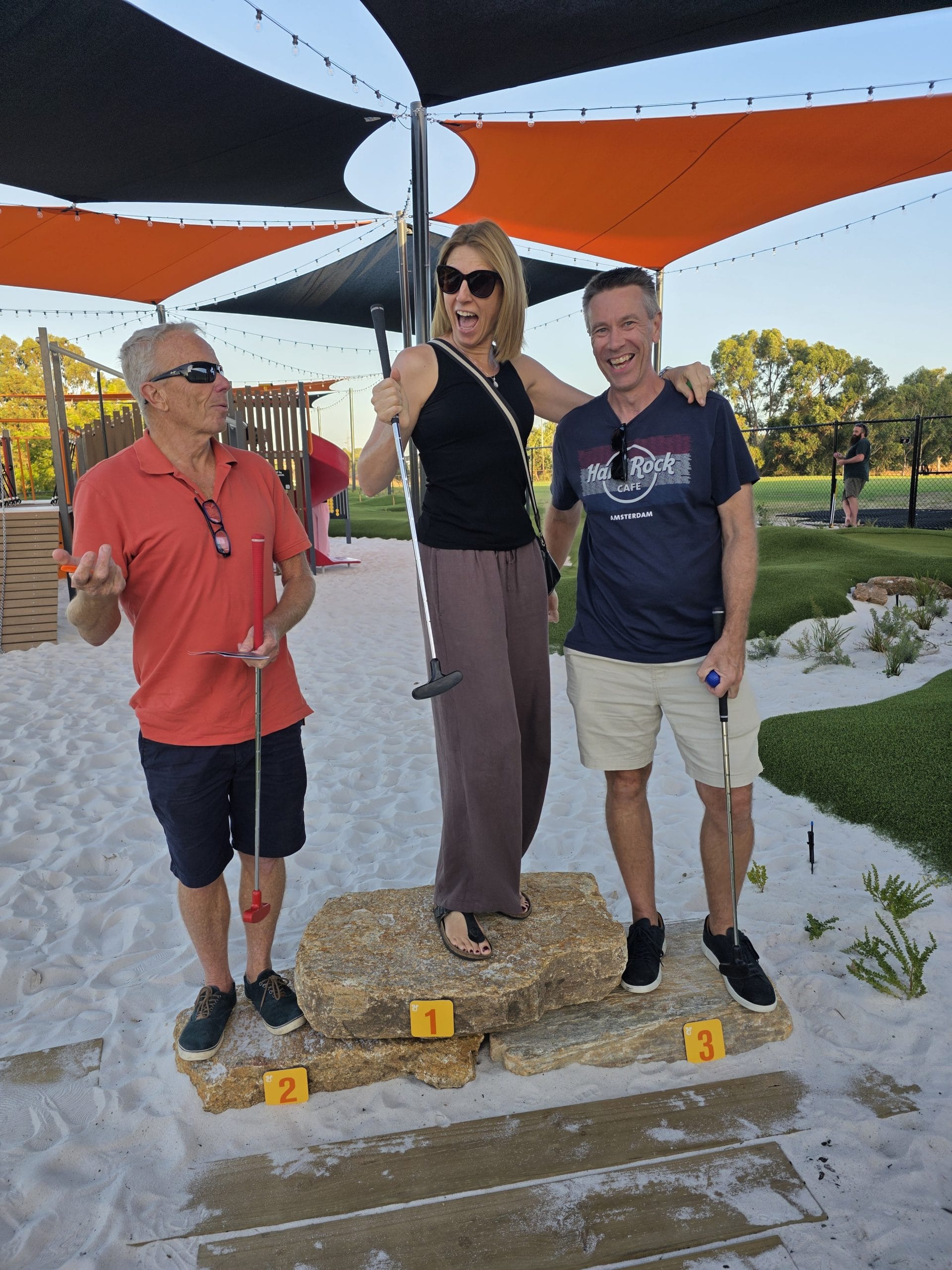 Adults standing on podium on the mini golf Child playing mini golf at OuttaBounds
