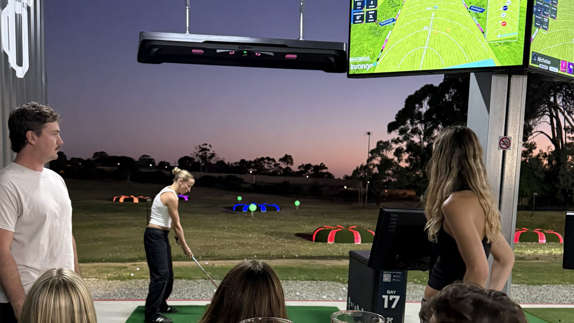 Player taking shot on outdoor golf driving range while technology tracks the shot
